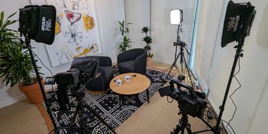 Cozy interview setup with cameras, lights, and two chairs around a coffee table.