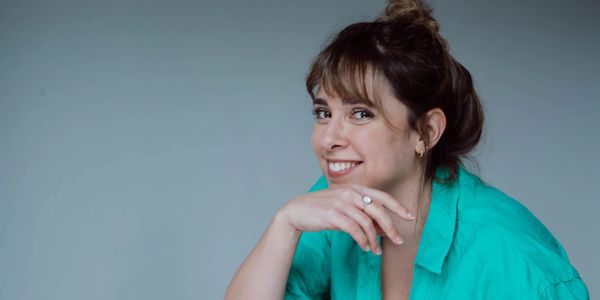 Smiling woman in a teal blouse with hand near face.
