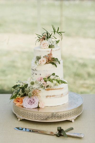 Elegant three-tiered semi-naked cake adorned with pastel flowers on a decorative stand.