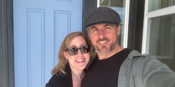 Smiling couple posing for a selfie outside a home with a blue door.