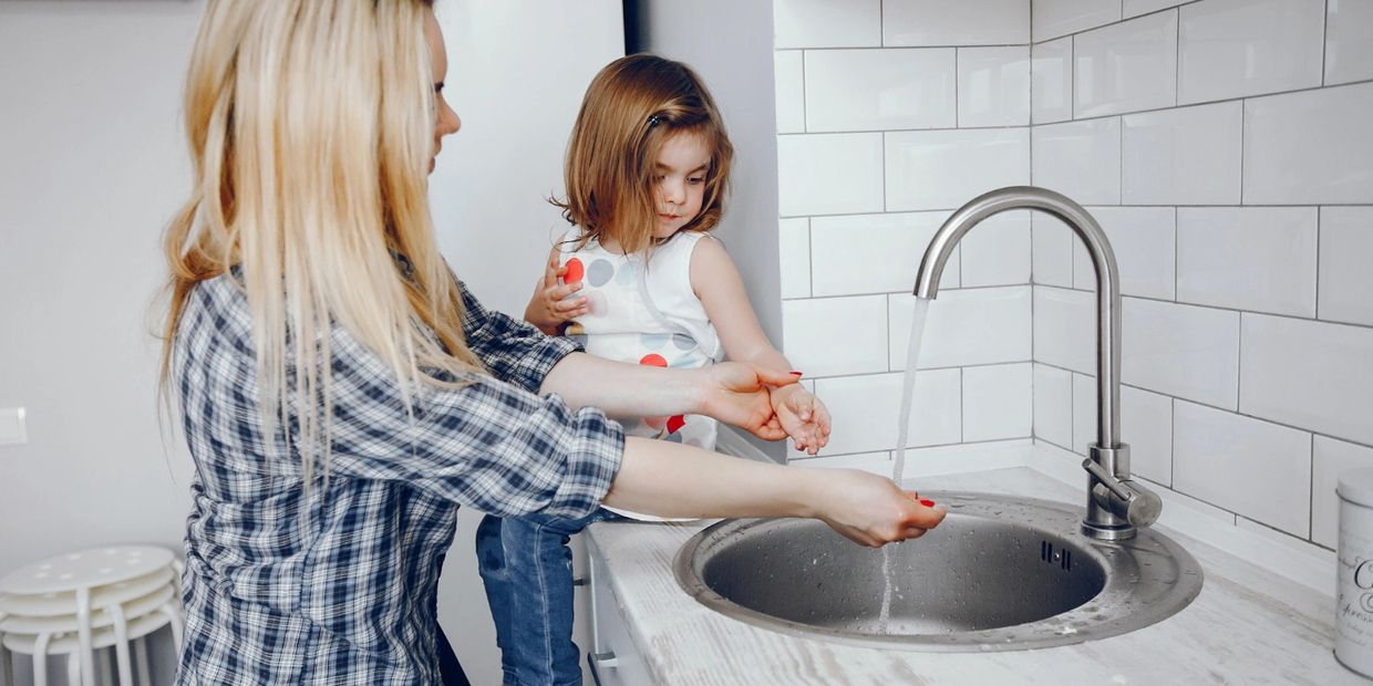 Woman shows child how to wash hands in sink