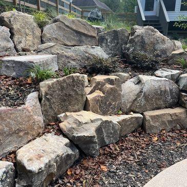 A stone retaining wall with rocks and some plants.