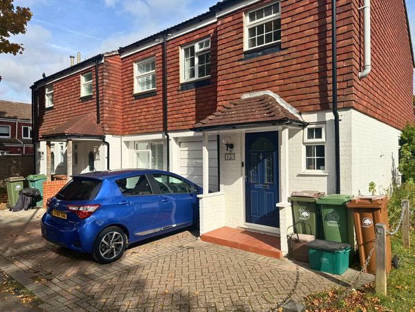 Blue car parked outside a red-brick and white house with bins.