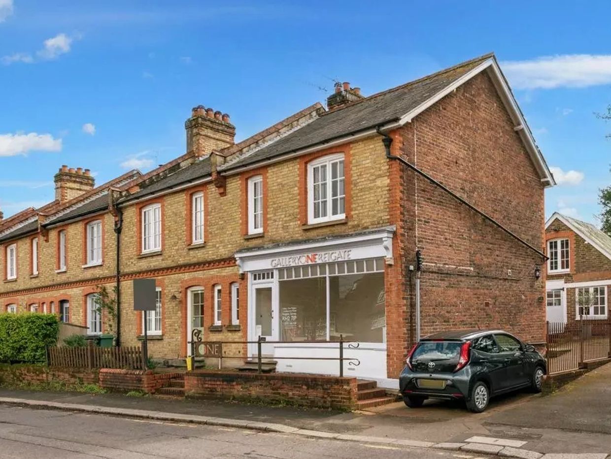 Row of brick townhouses with a small gallery storefront and parked cars.