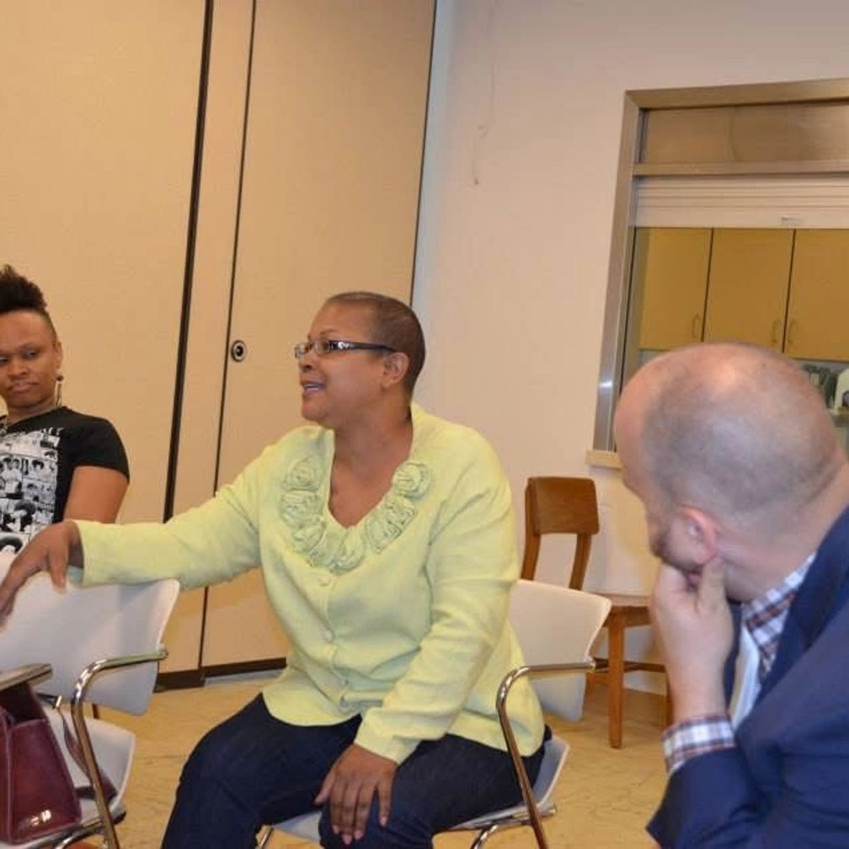 Three people engaged in a discussion in a casual meeting room.