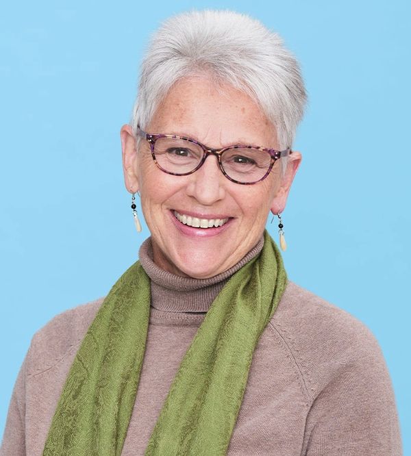 Smiling elderly woman with white hair and glasses against a blue background.