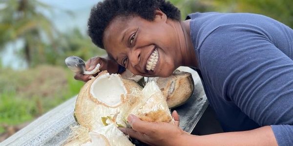 A smiling person eating fresh coconut outdoors.