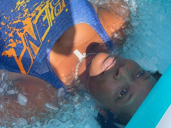 A woman submerged in an ice-filled pool wearing a blue tank top.