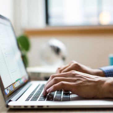 Hands typing on a laptop keyboard in a bright room.