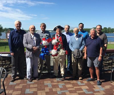 Group of men posing outdoors with a man in a patriotic outfit holding a wreath.