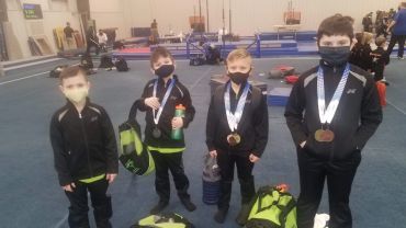 Four young boys wearing medals and face masks at a sports gym.