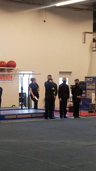 Four people standing in a gym or training area wearing black clothing.