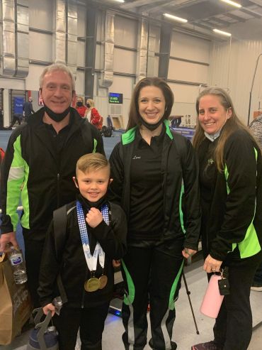 Four people in sportswear posing indoors, a child with medals around his neck.