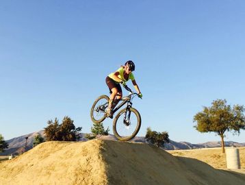 Person performing a jump on a mountain bike over a dirt mound.