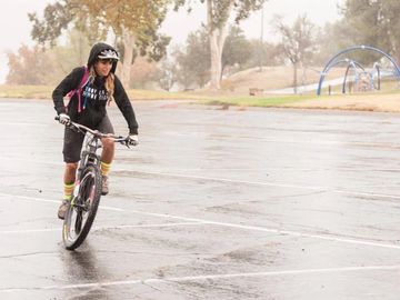 Person riding a bike in a wet parking lot on a cloudy day.