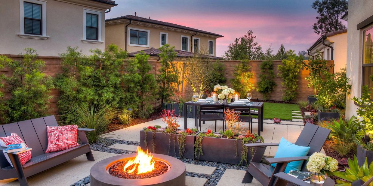 A landscaped backyard with spruces, fences, patio paver stones, fire pit, and rocks
