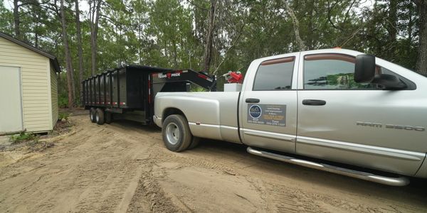 Silver RAM 3500 truck towing a black Texas Pride trailer in a forested area.