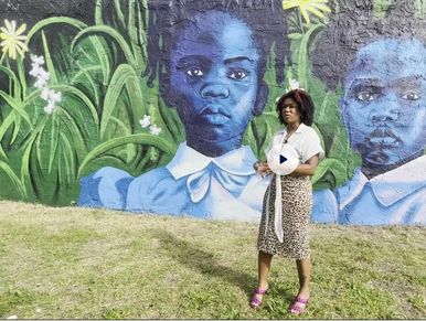 Woman standing beside mural of blue-painted girls.
