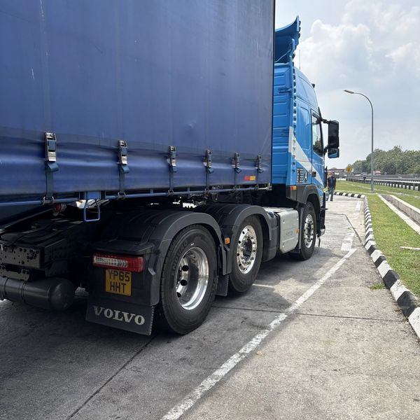 A blue Volvo truck parked on the roadside under a cloudy sky.