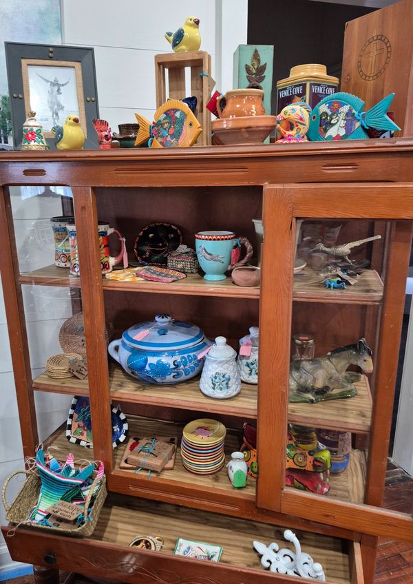 Wooden cabinet filled with colorful ceramic and pottery items including birds, fish, and kitchenware.