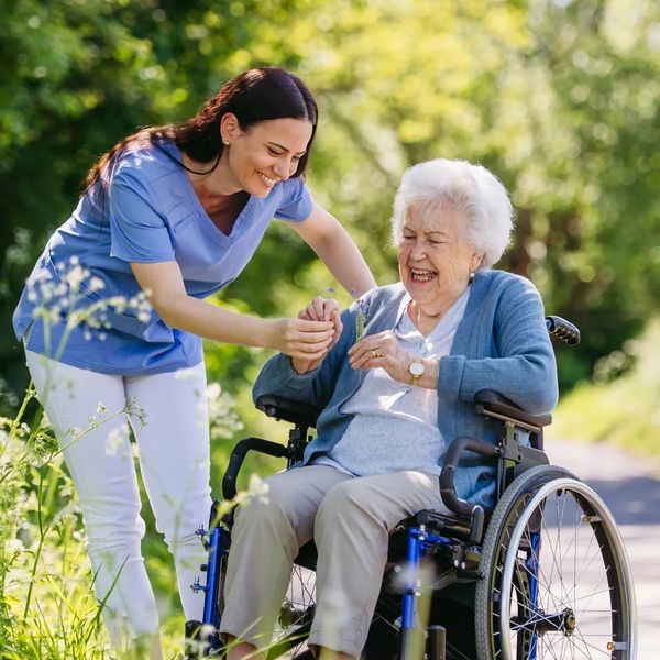 Caregiver and elderly woman in a wheelchair enjoying flowers outdoors.
