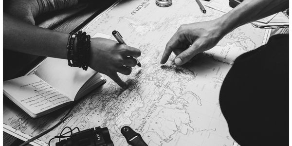 Image of a map with two people looking at it; one hand is pointing at a location; the other is holdi