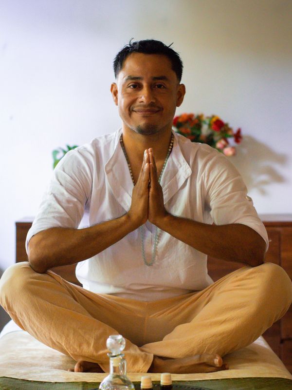Man sitting cross-legged with hands in prayer gesture, smiling peacefully.