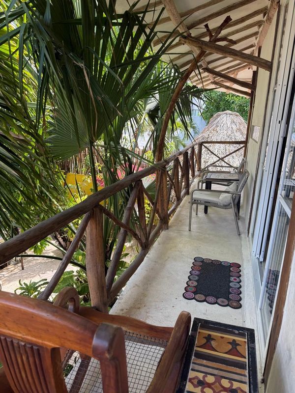 Cozy balcony with wooden railings and chairs surrounded by tropical greenery.