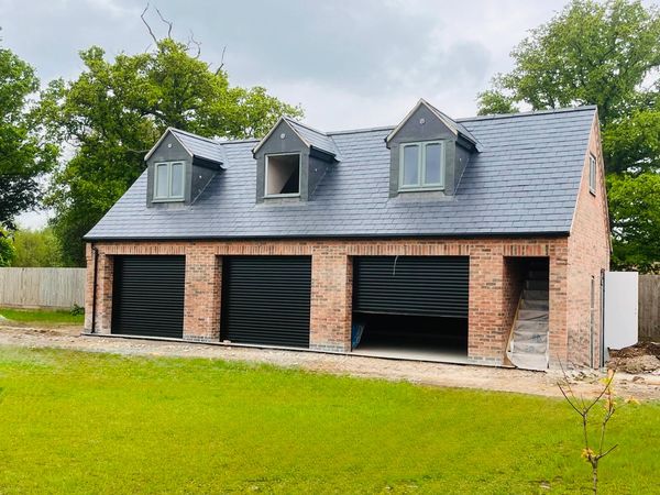 Brick garage with three black doors and dormer windows on the roof.