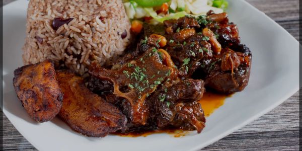 Plate with rice and peas, fried plantains, stewed meat, and mixed vegetables.
