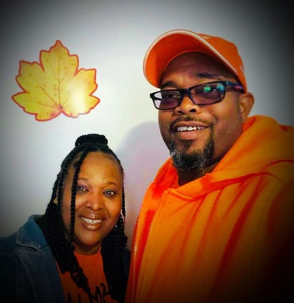 A smiling couple posing together indoors with a decorative leaf on the wall.