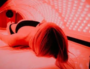 Person lying inside a red-lit tanning bed.