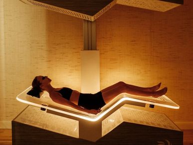Woman relaxing on a glowing spa bed in a warm, ambient room.