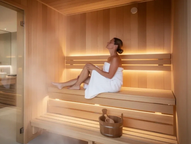 Woman relaxing in a wooden sauna wrapped in a white towel.