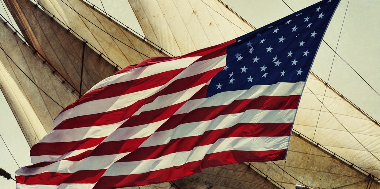 American flag waving in front of ship sails.