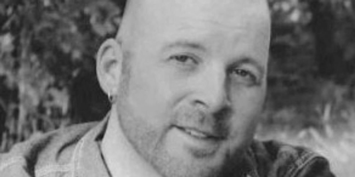 Black-and-white close-up portrait of a smiling bald man with an earring.