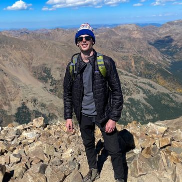 Man standing on rocky mountain peak under clear blue sky.