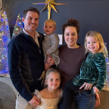 A happy family of five posing indoors with festive holiday decorations.