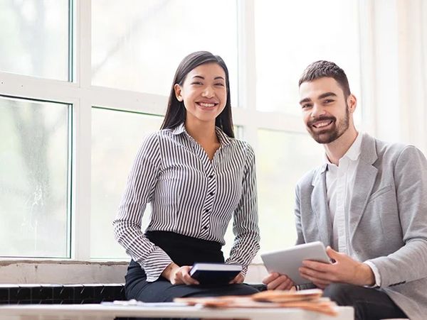 Two colleagues smiling with tablet and notebook in a bright office.