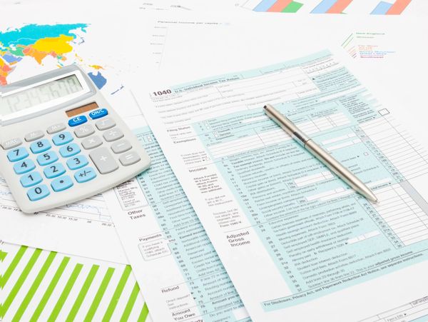 Calculator, pen, and tax forms on financial charts and graphs.