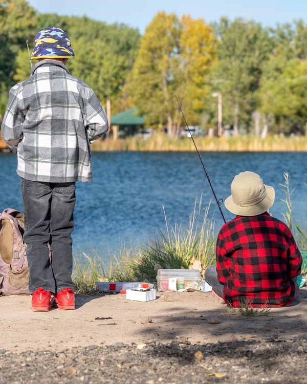 Two children fishing by a lake on a sunny day.