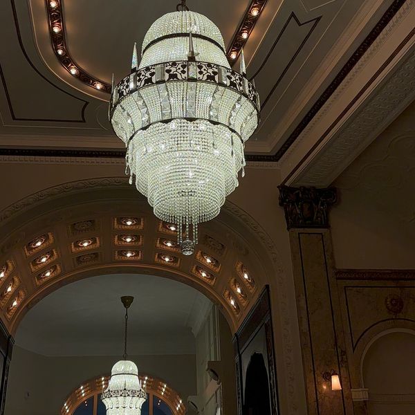 Elegant crystal chandeliers illuminate a grand, ornately decorated hallway.