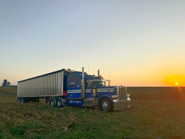 Blue Hoker truck and trailer in the fields with sun coming up