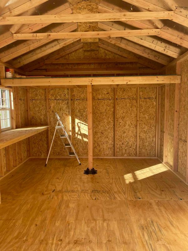Interior of a wooden shed under construction with a ladder and sunlight.