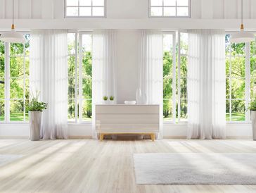 
A clean and spacious sunroom with large windows, white curtains, and minimalist furniture.