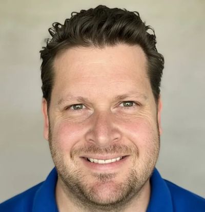 Smiling man with curly hair and a blue shirt.