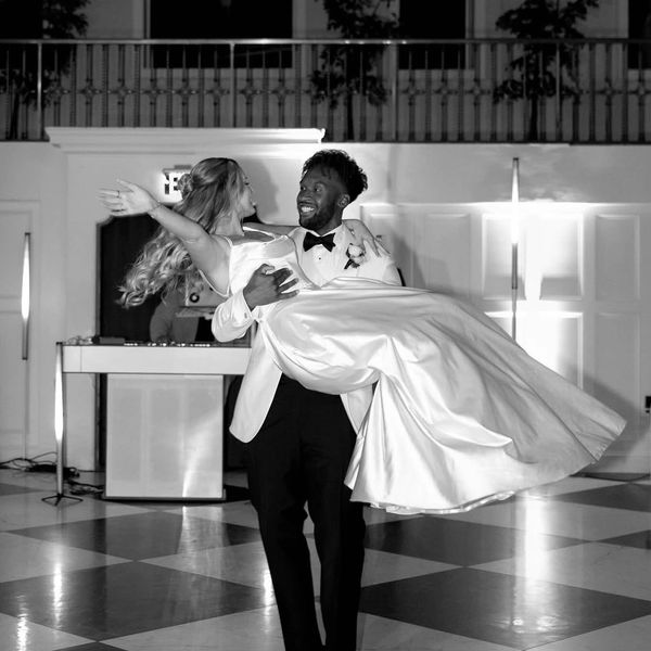 Groom joyfully carries bride on a checkered floor at wedding.