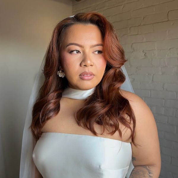Woman with styled auburn hair in a white strapless dress.