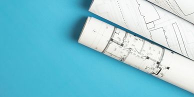 Building drawings are rolled up to show CAD Drafting completed, over a blue background