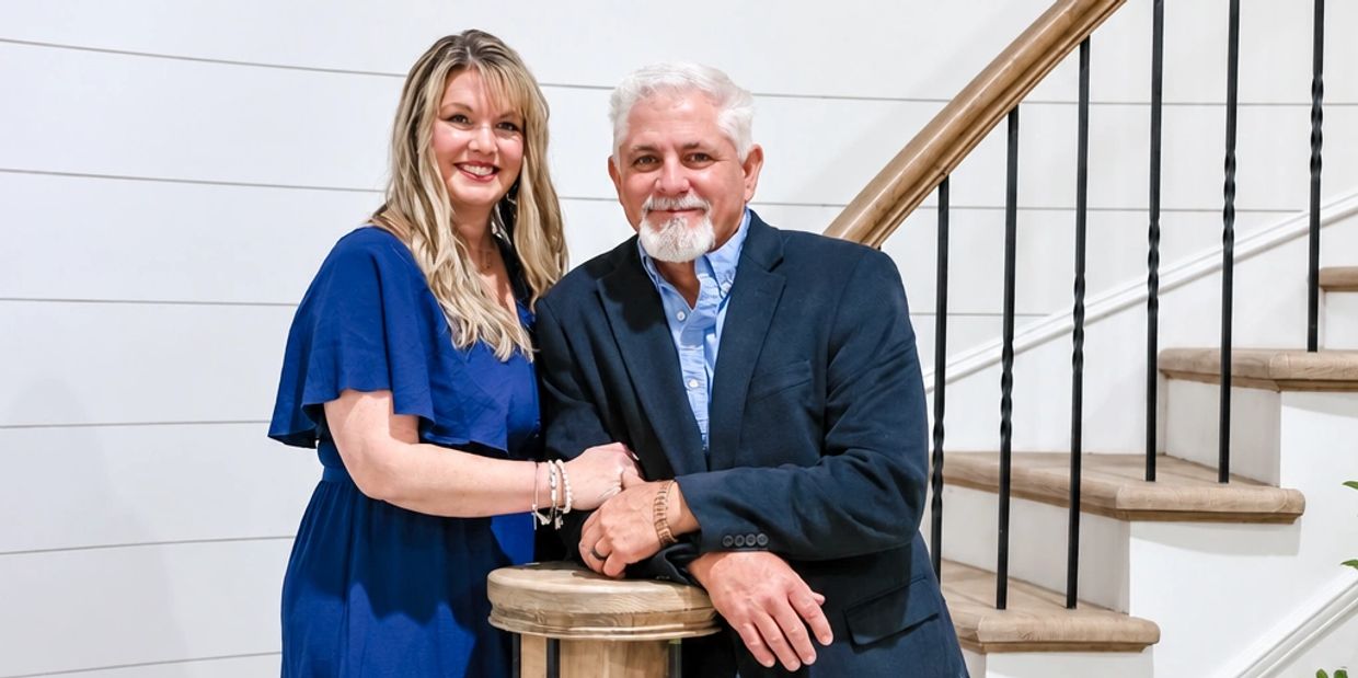 Smiling couple posing indoors by stairs.